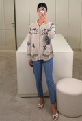 Person wearing a patterned cardigan and blue jeans taking a mirror selfie.