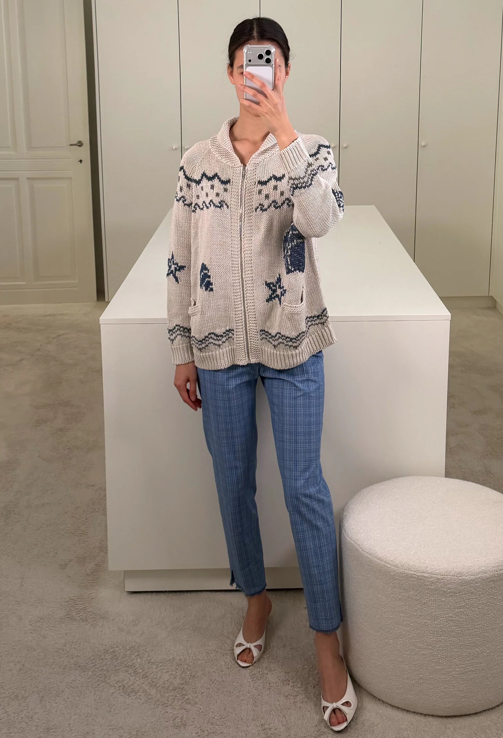 Person wearing a patterned cardigan and blue jeans taking a mirror selfie.