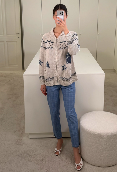 Person wearing a patterned cardigan and blue jeans taking a mirror selfie.
