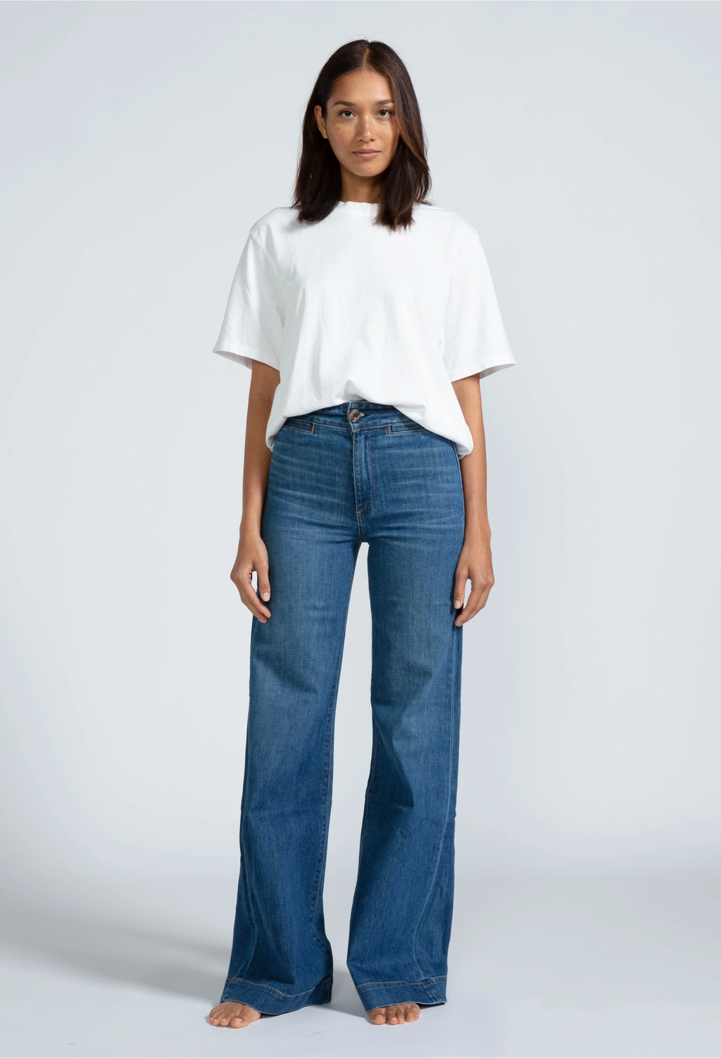 a woman wearing a white t-shirt and high waisted dark wash jeans. white background.