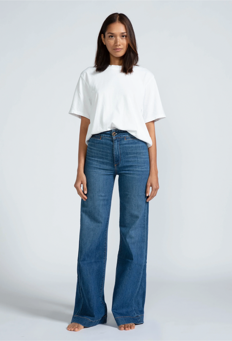a woman wearing a white t-shirt and high waisted dark wash jeans. white background.