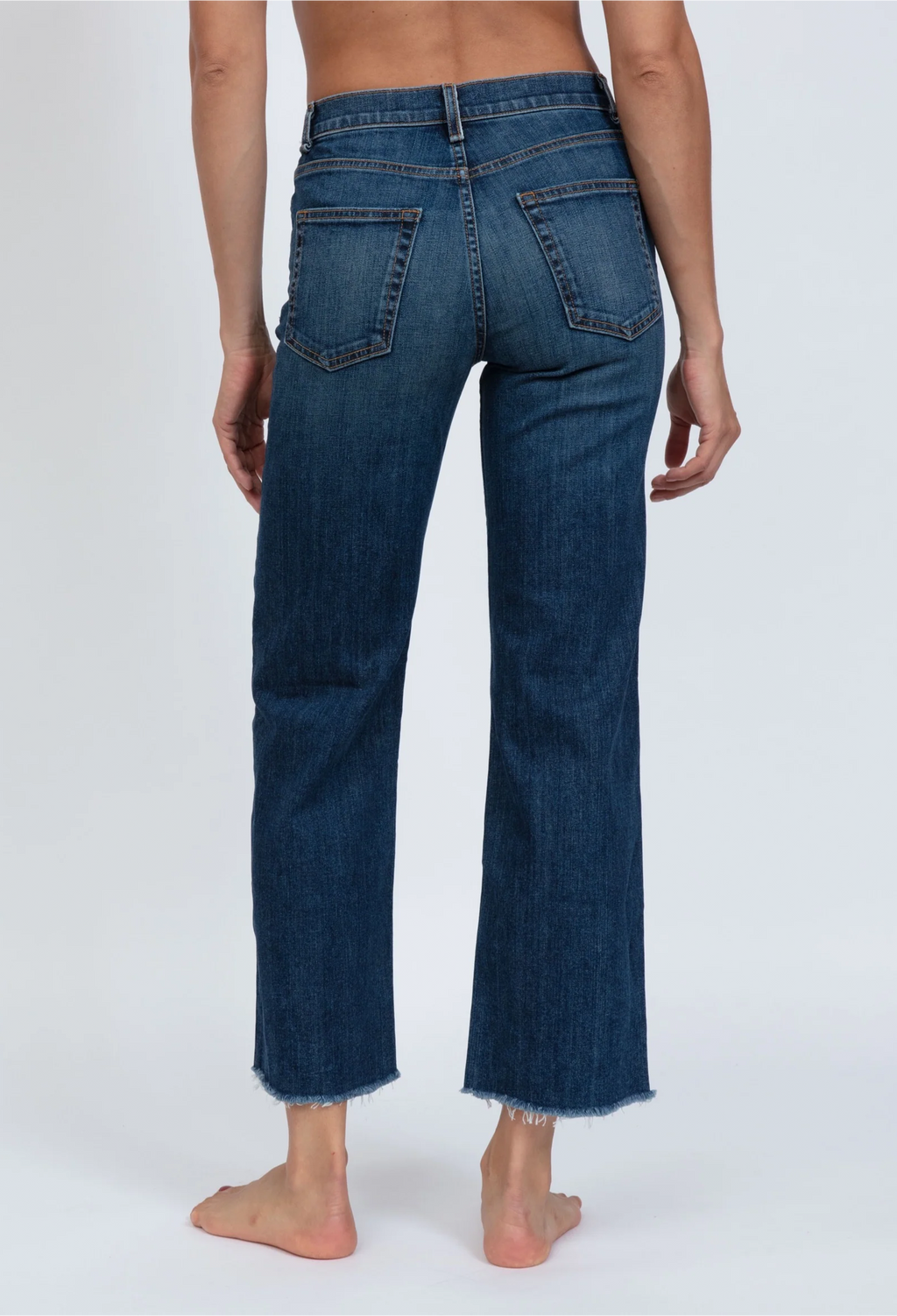 Backside of model wearing high rise wide leg cropped medium wash jeans with frayed hem and back pockets. She stands in front of a white background. 