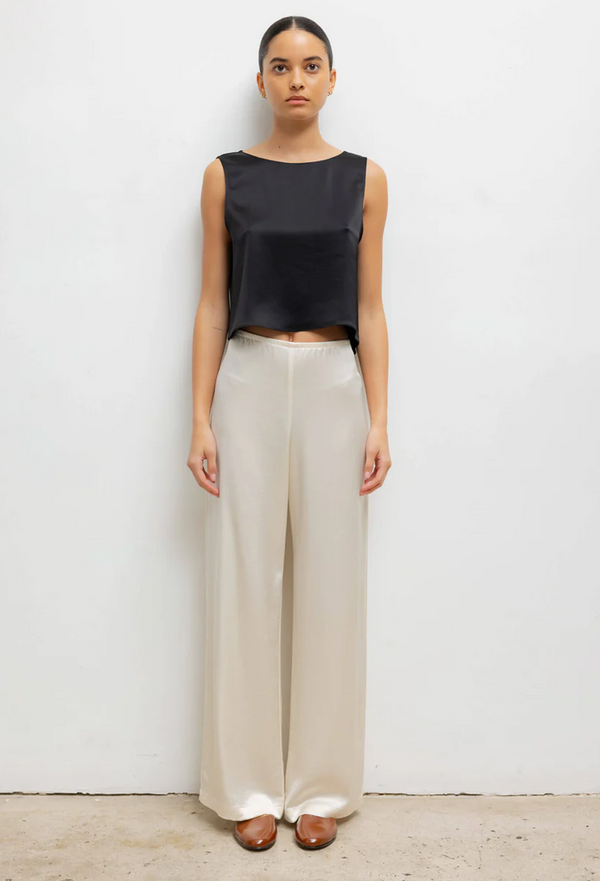 Woman wearing a black sleeveless top and beige wide-leg pants on a white background
