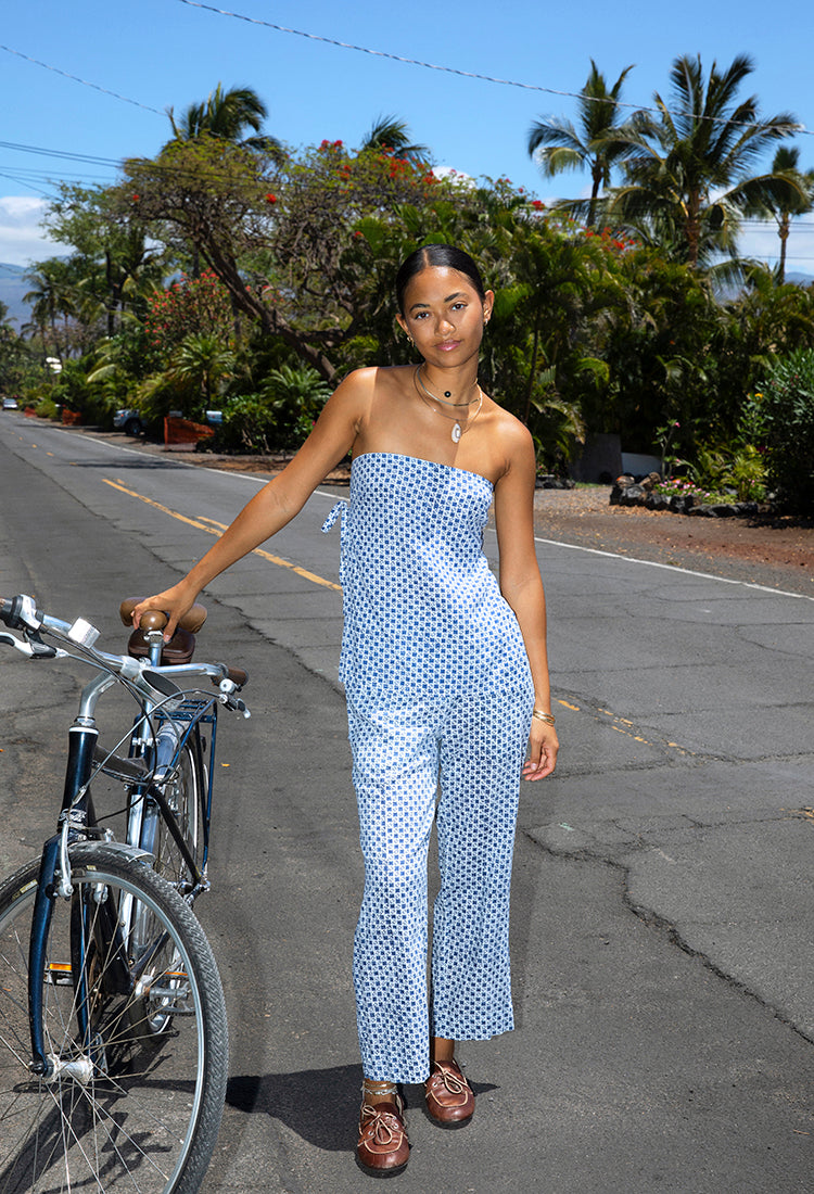 Model wears navy and white block printed cotton-linen blend straight leg pant with matching tube top and brown loafers. She stands next to a bike with a tropical background. 