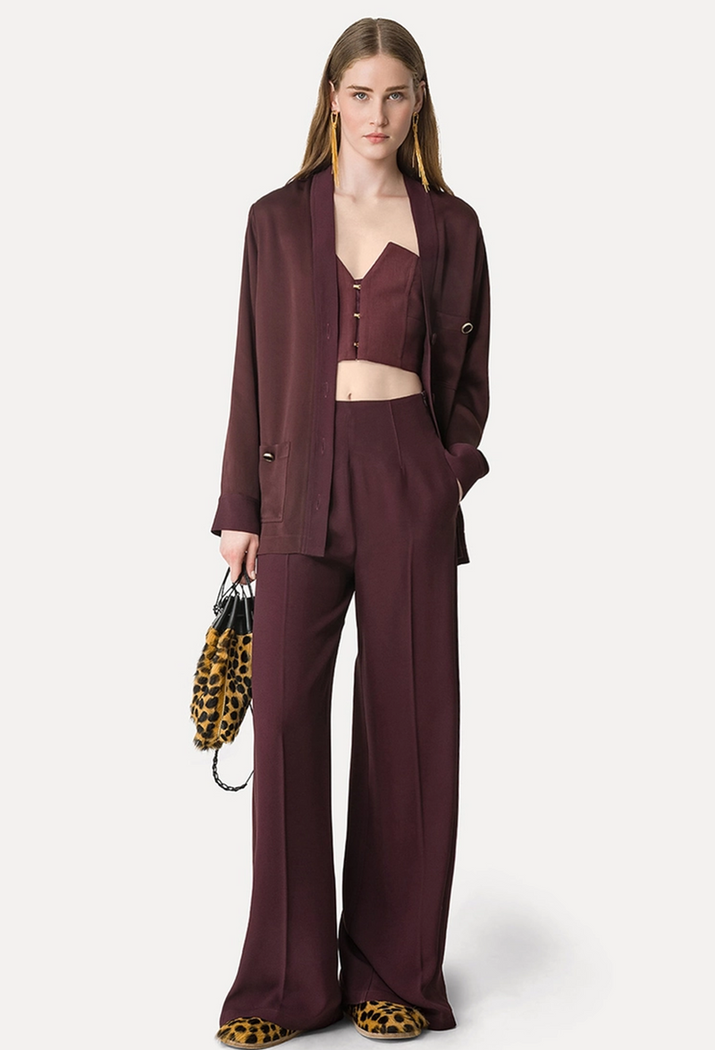 Woman wearing a burgundy suit holding a leopard print bag on a white background