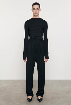 Model wears black long sleeve lightweight cashmere jersey sweater with black pants and black shoes. She stands in front of a white wall. 