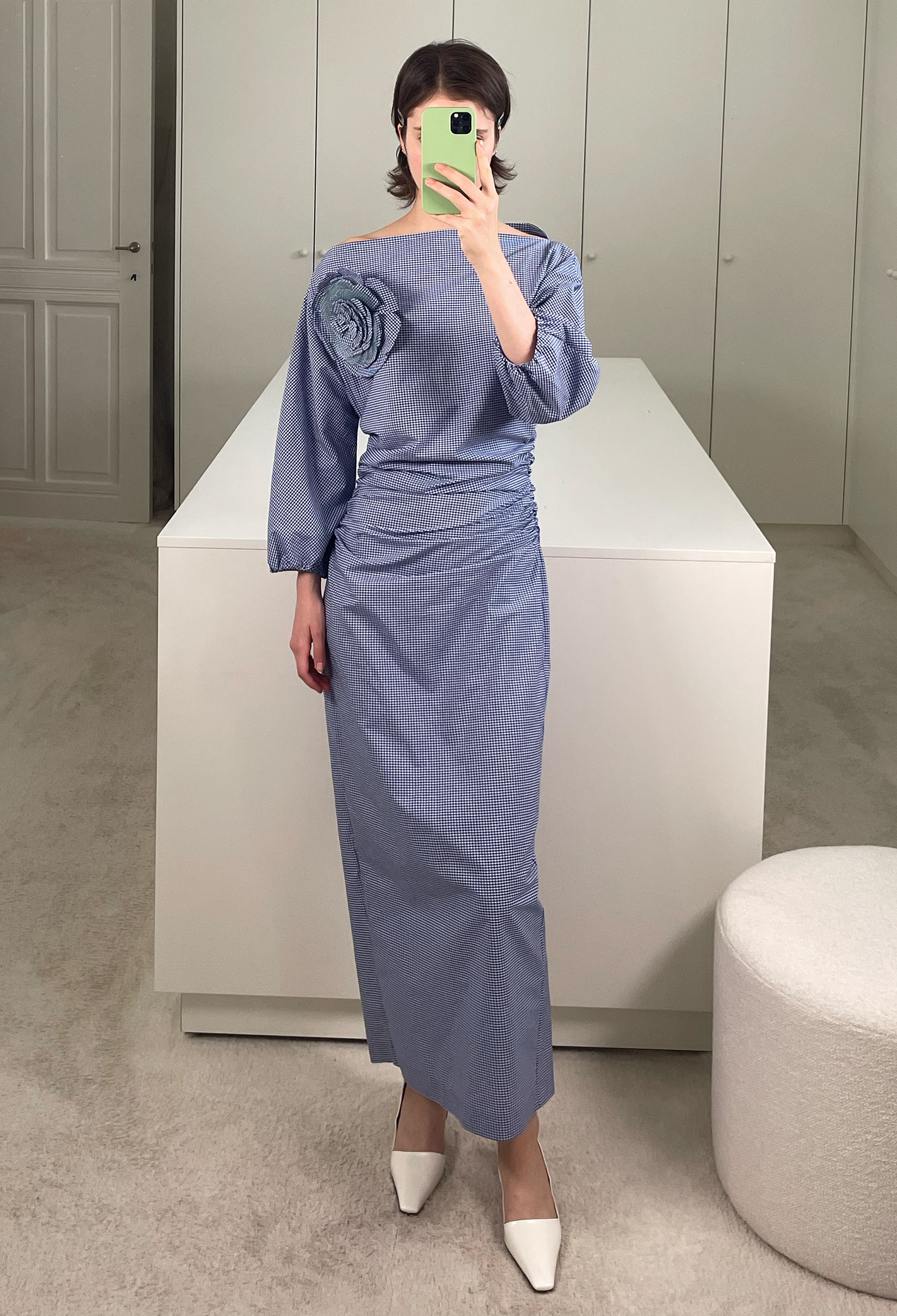 Woman taking a mirror selfie wearing a blue dress in a minimalistic room.