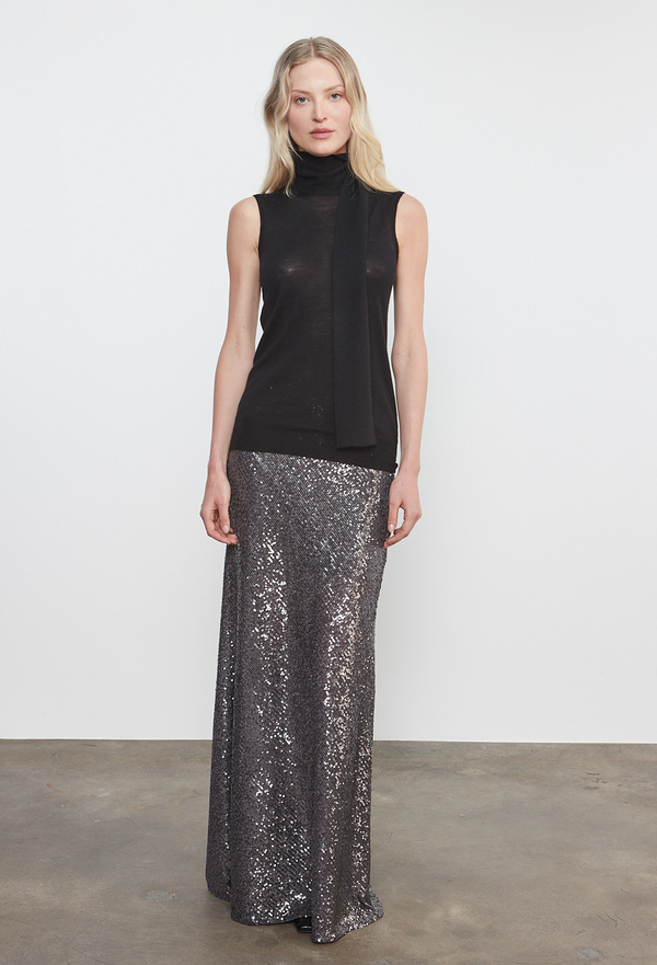 Woman wearing a black sleeveless top and silver sequin skirt on a white background