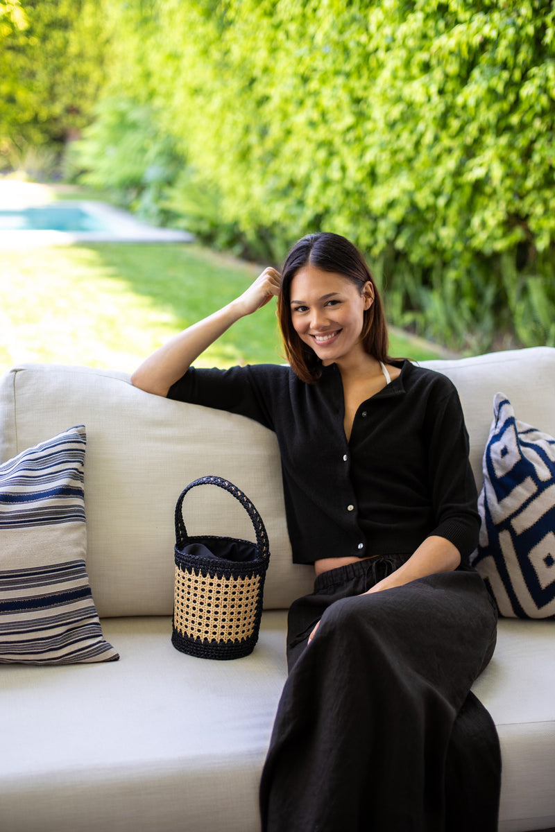a model sitting on an outdoor couch wearing a black cardigan and a black skirt.