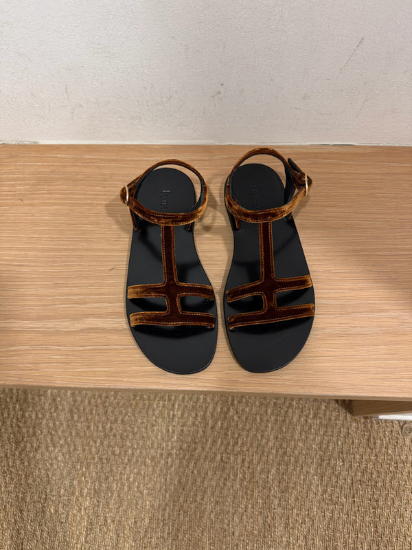 Rust color suede sandals side by side on a bench in a dressing room. 