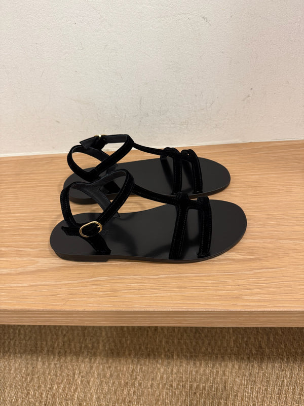 Black suede sandals side by side on a bench in a dressing room. 
