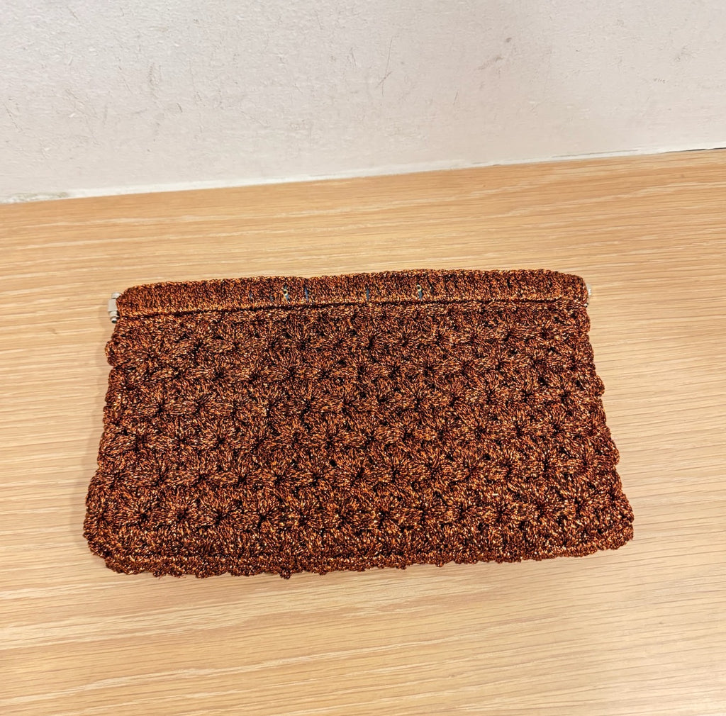 CLUTCH ON A WOOD BACKGROUND. THE CLUTCH IS TEXTURED AND IS THE COLOR RUST