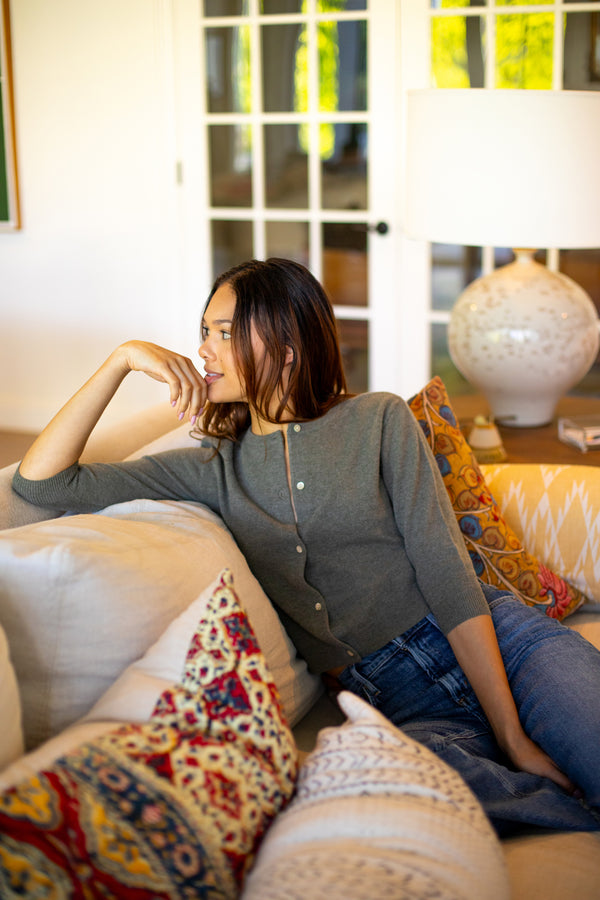 a model sitting on a couch in a living room wearing a grey cardigan.