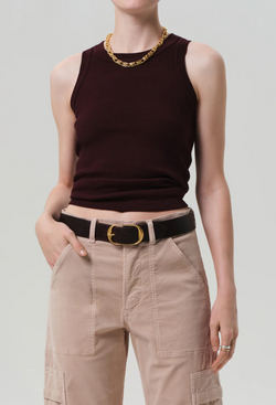 Person wearing a dark sleeveless top and beige pants with a gold belt on a light gray background