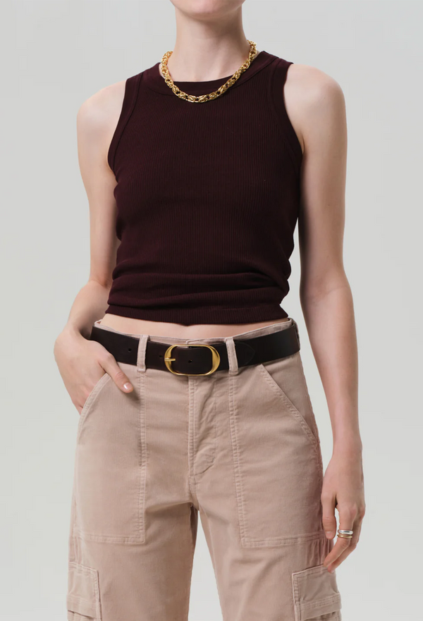 Person wearing a dark sleeveless top and beige pants with a gold belt on a light gray background