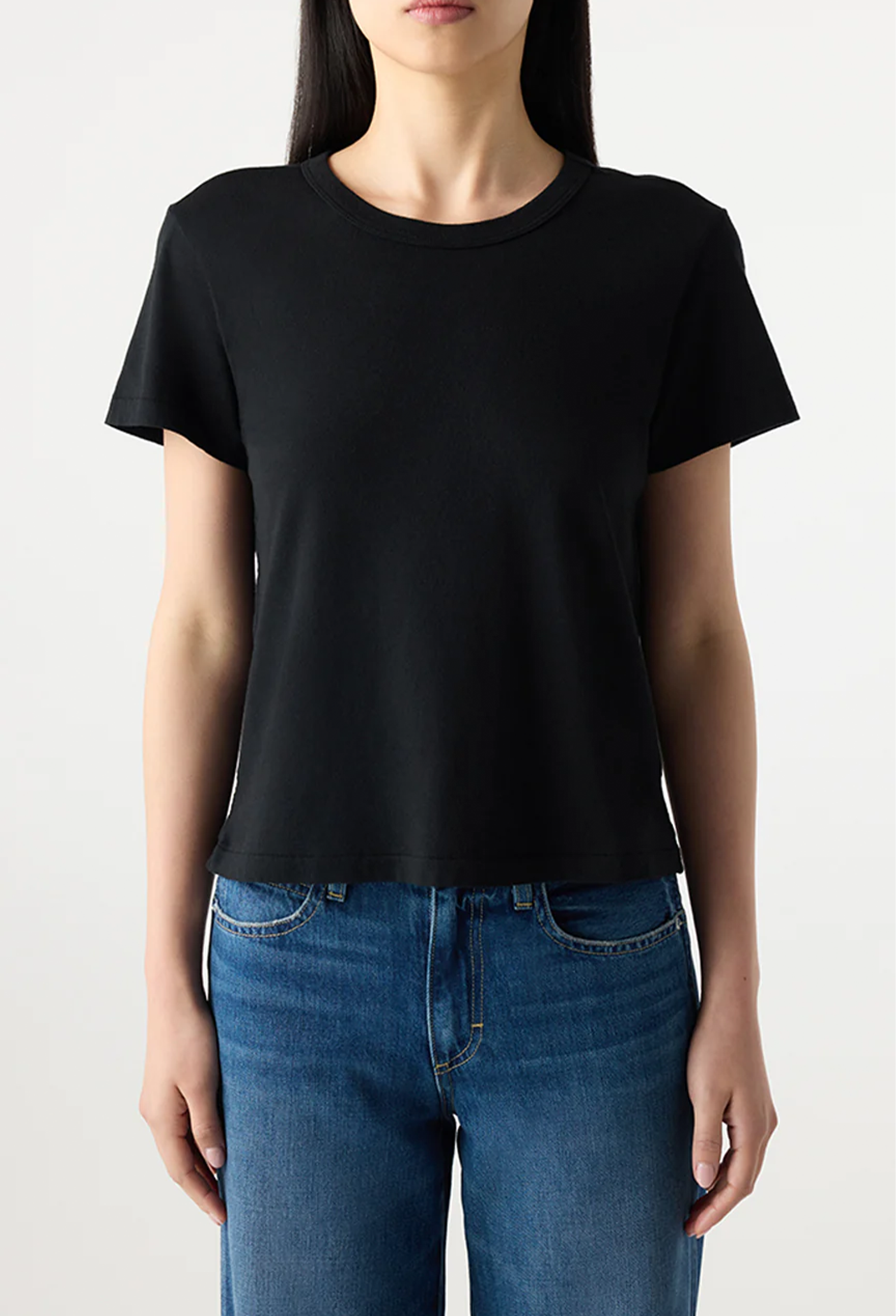 Person wearing a black t-shirt and blue jeans on a plain background