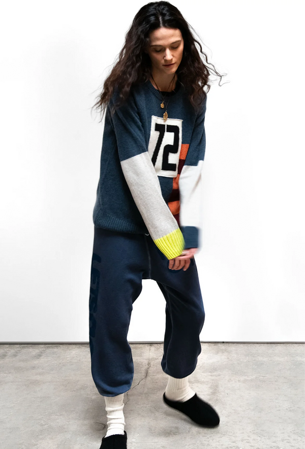 Person wearing a colorful sweater and blue sweatpants on a plain background