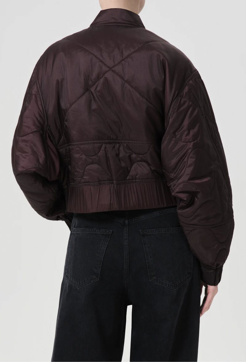 a model wearing a puffy bomber jacket with seam embellishments on a white background.