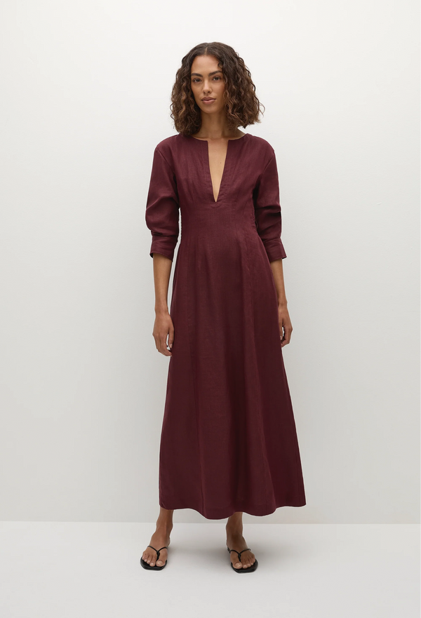 a model wearing a midi burgundy dress with 3/4 sleeves and a deep v-neck. white background.