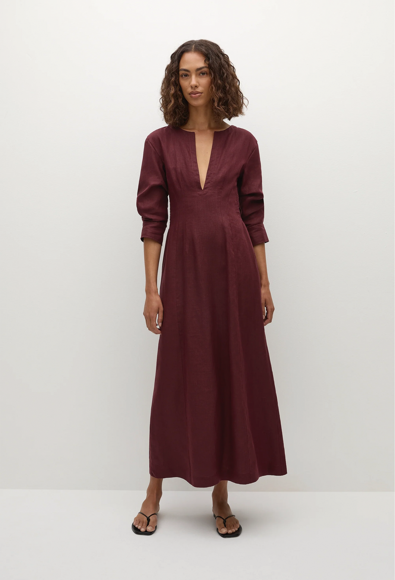 a model wearing a midi burgundy dress with 3/4 sleeves and a deep v-neck. white background.