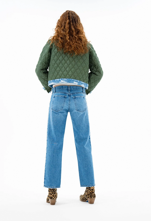 Person wearing a green quilted jacket and blue jeans from behind on a white background