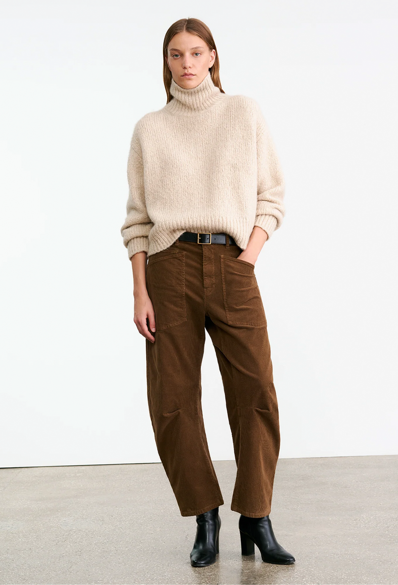 Woman wearing a cream sweater and brown corduroy pants on a white background