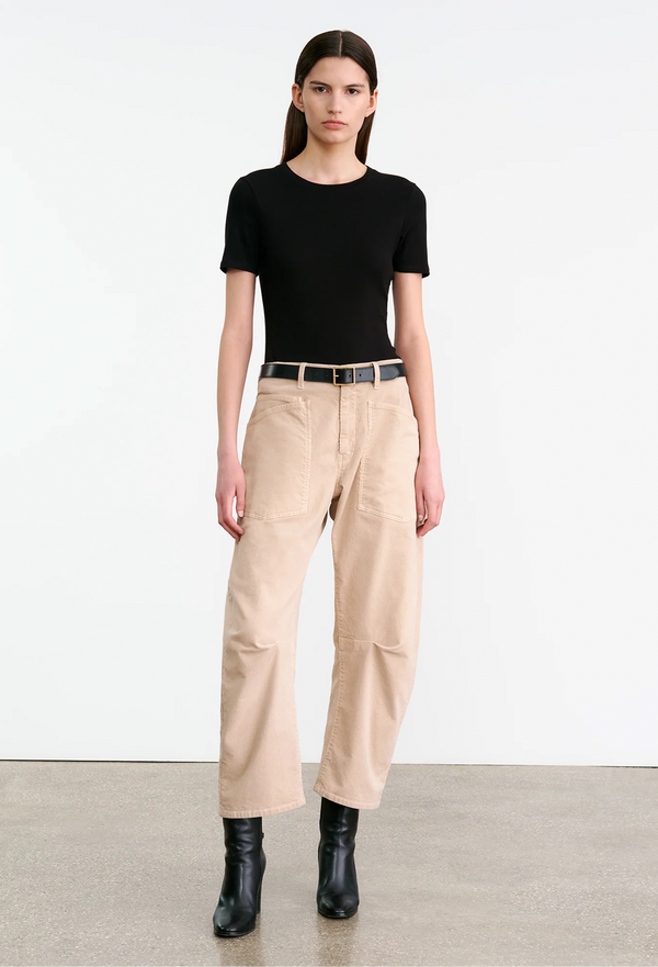 Person wearing a black top and light blush corduroy pants with a belt on a white background
