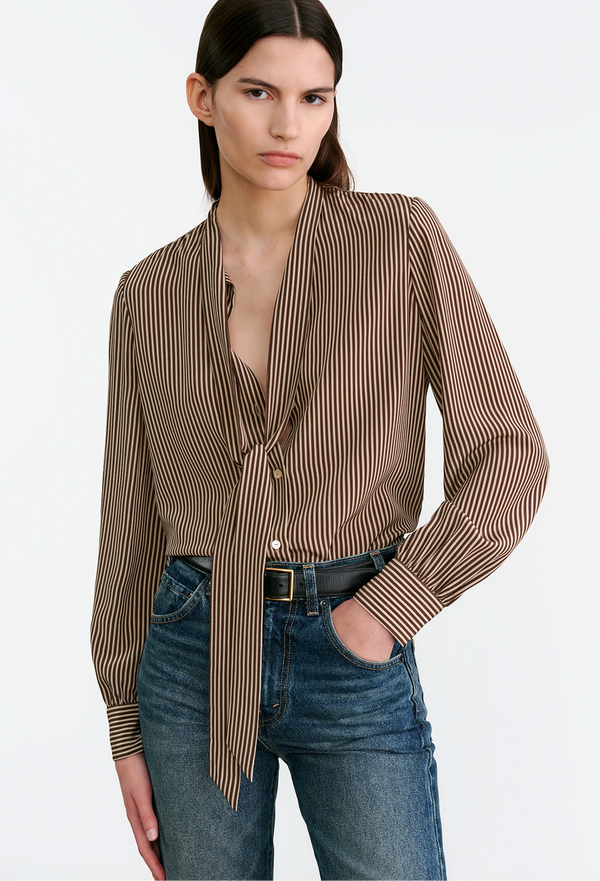 Woman wearing a brown striped blouse and blue jeans on a white background