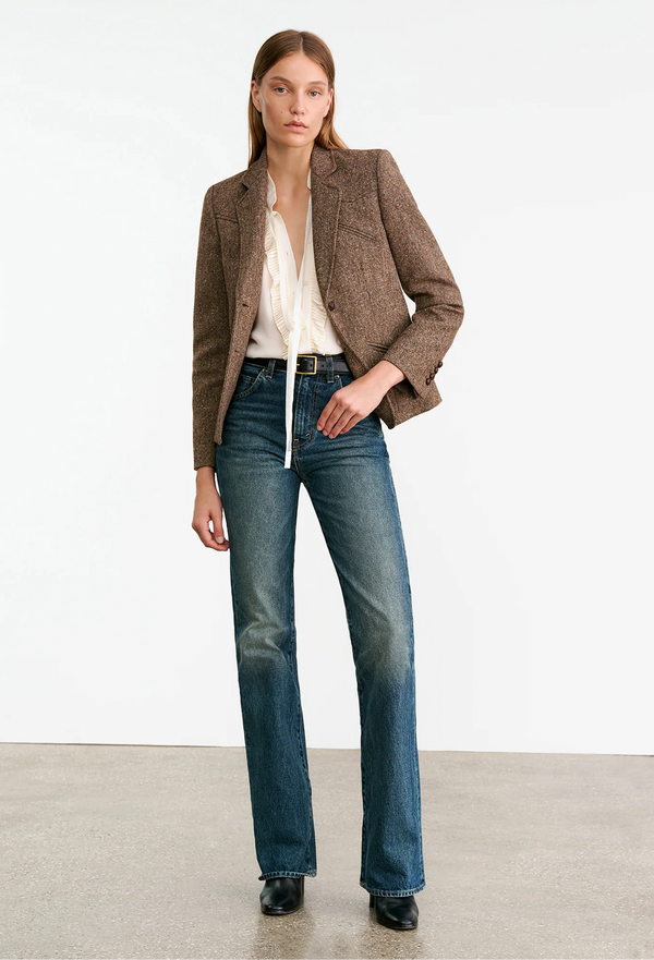 Woman wearing a brown blazer, white shirt, and blue jeans on a white background