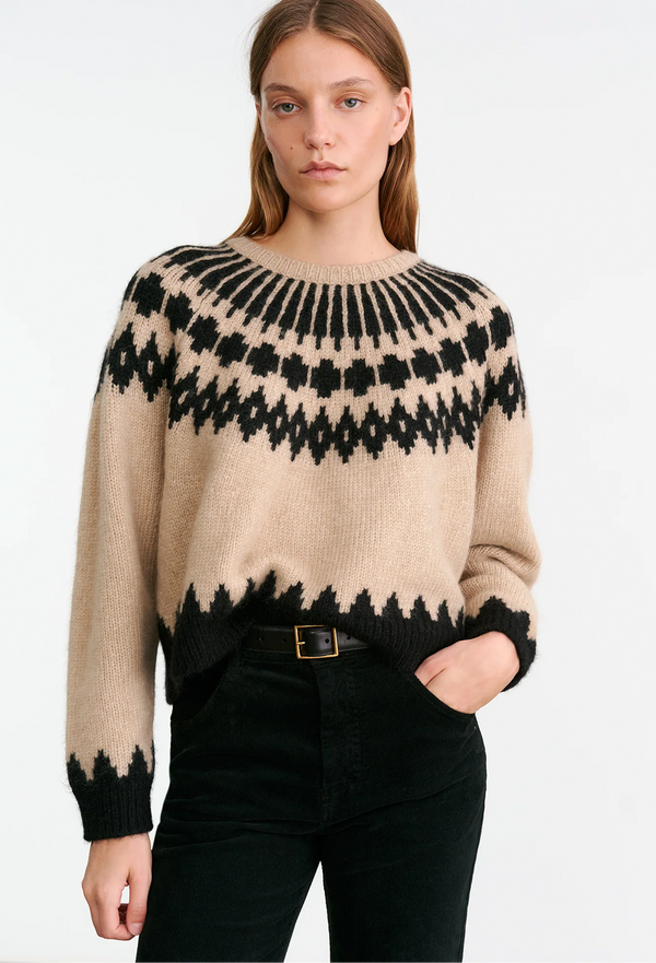 Woman wearing a beige sweater with black fair isle pattern on a white background