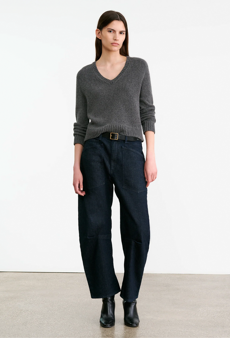 Woman wearing a gray sweater and dark pants on a white background