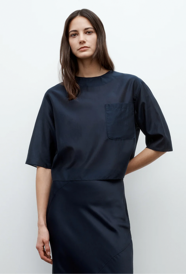 Person wearing a navy blue shirt and skirt with a plain background