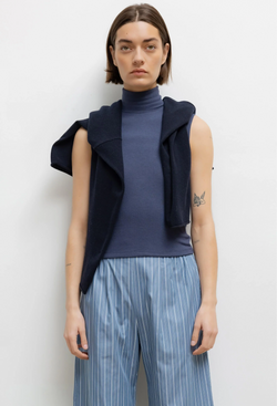 Person wearing a sleeveless blue turtleneck and striped pants on a white background