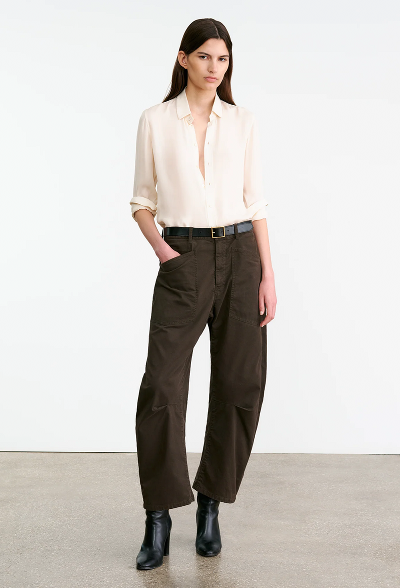 Woman wearing a white blouse and brown pants on a plain background