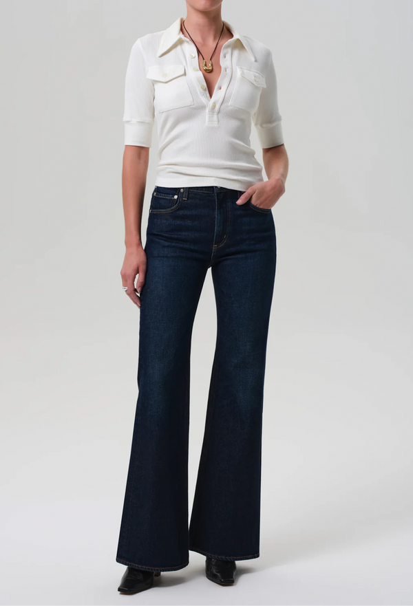 Person wearing a white blouse and dark blue flared jeans on a plain background
