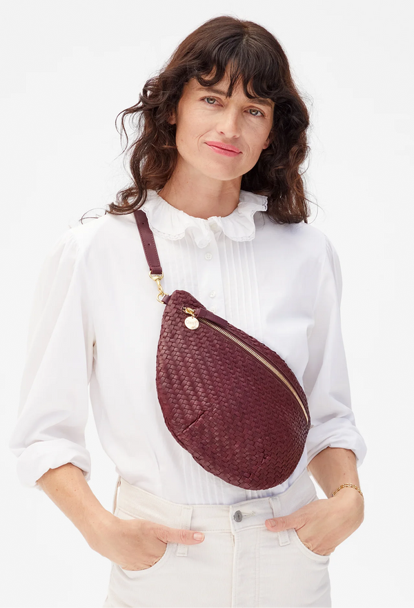 Woman wearing a maroon woven waist bag on a white background