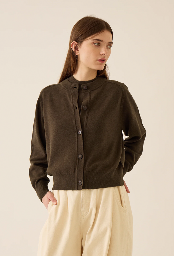 Woman wearing a brown cardigan with beige pants on a beige background