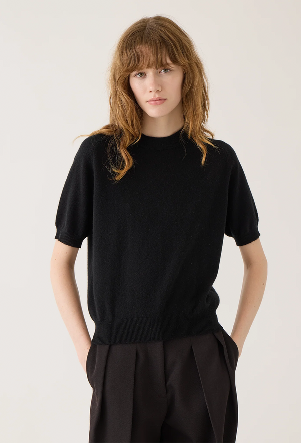 Person wearing a black short sleeve sweater and pants on a plain background