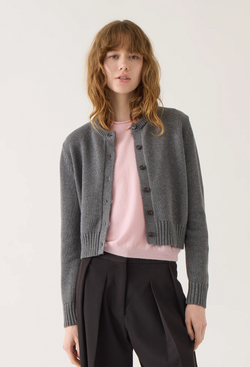 Woman wearing a gray cardigan over a pink shirt with black pants on a white background