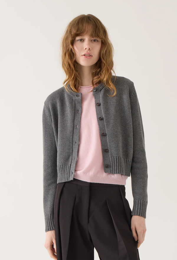 Woman wearing a gray cardigan over a pink shirt with black pants on a white background