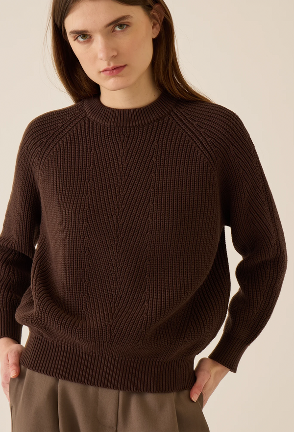 Woman wearing a brown sweater against a plain background