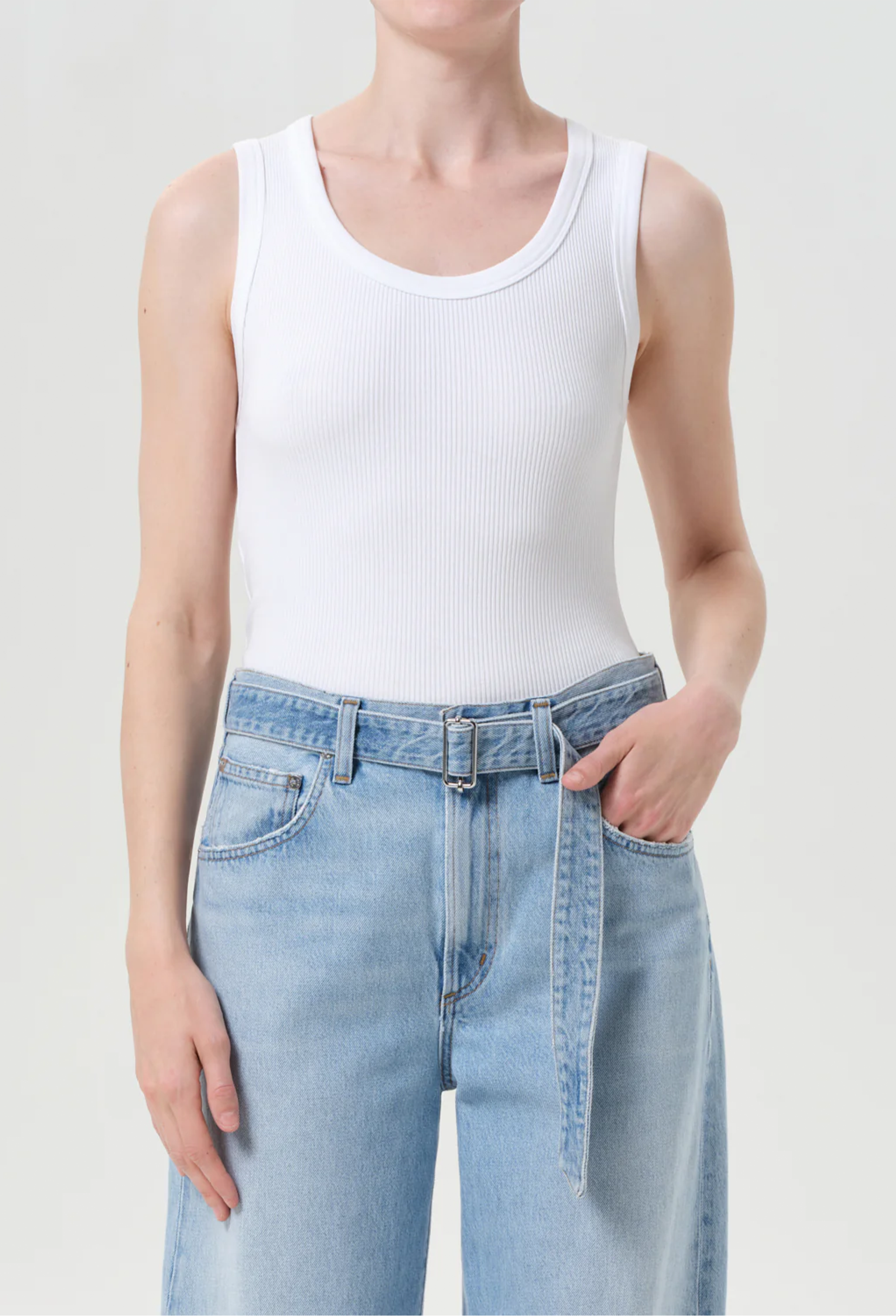 Person wearing a white tank top and light blue jeans on a plain background