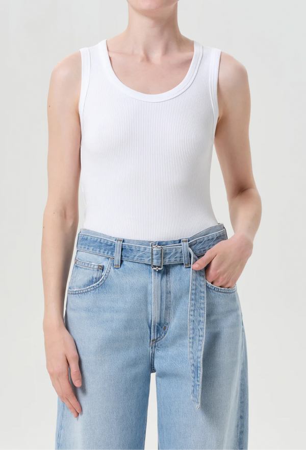 Person wearing a white tank top and light blue jeans on a plain background