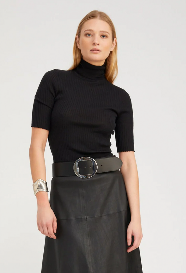 Woman wearing a black turtleneck and black skirt with a belt on a white background