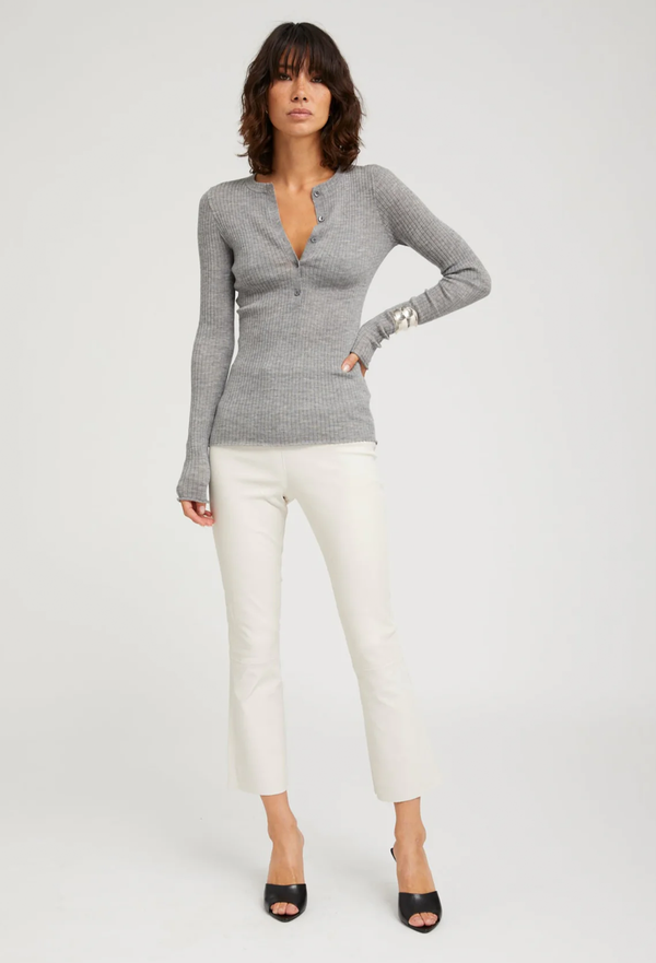 Woman wearing a gray henley sweater and white pants on a light gray background