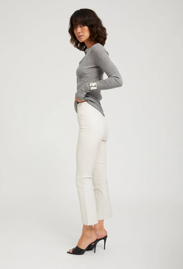 Woman wearing a gray sweater and white pants on a plain background