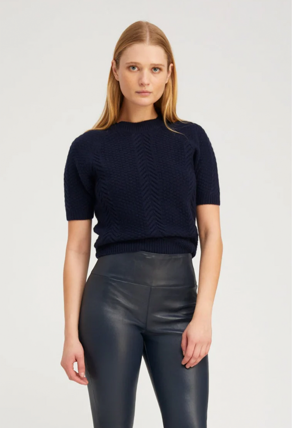 Woman wearing a navy sweater and black leather pants on a light gray background