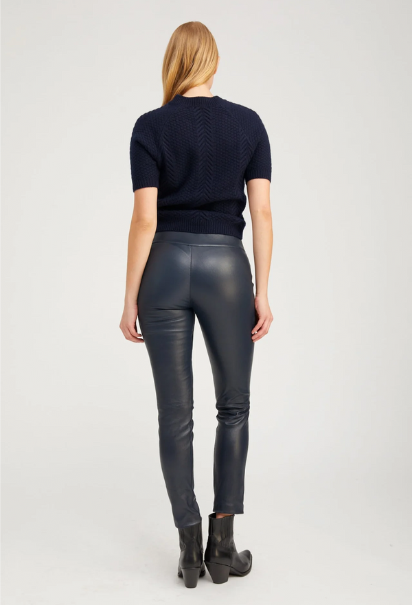 Person wearing a navy sweater and black leather pants on a white background