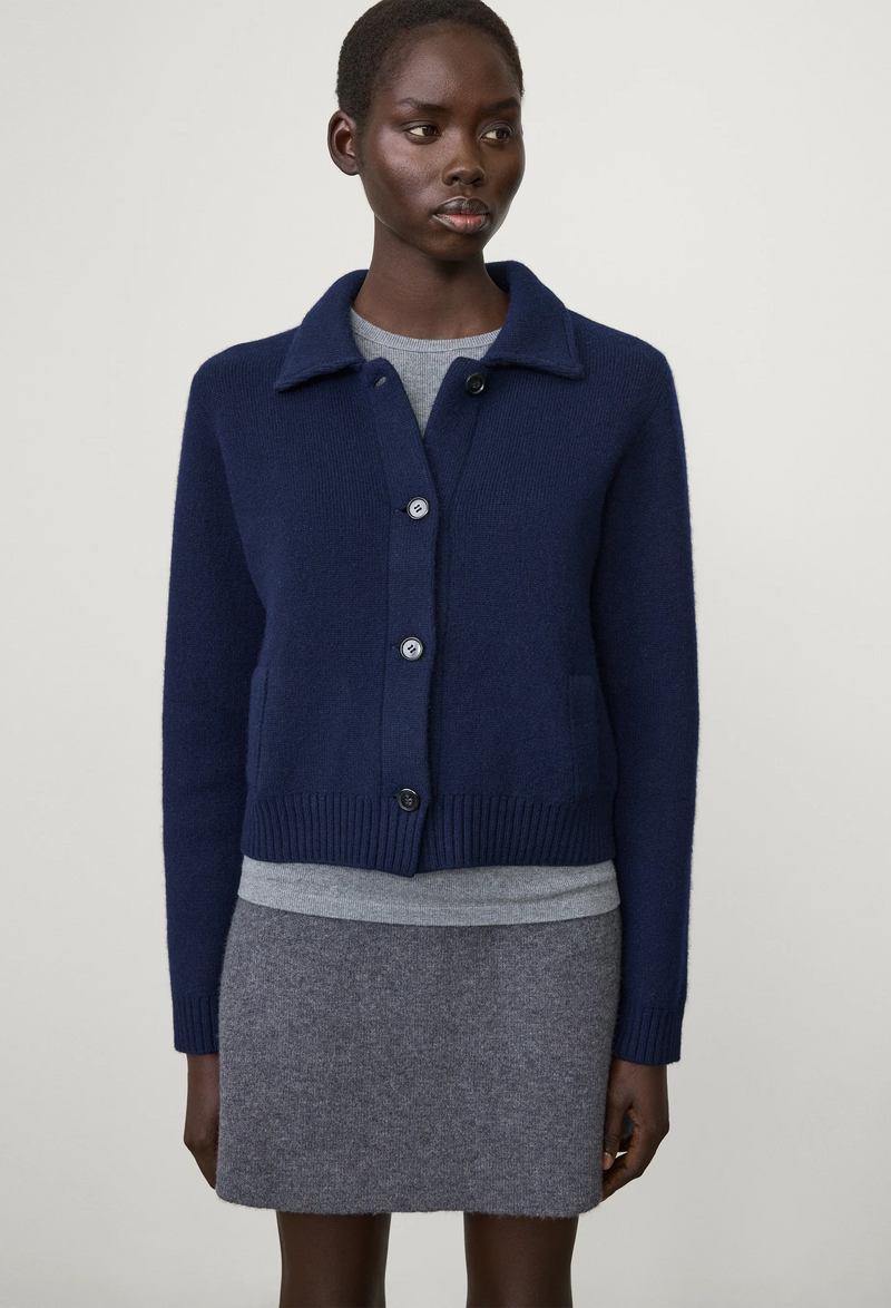 Person wearing a navy blue cardigan over a gray outfit on a white background
