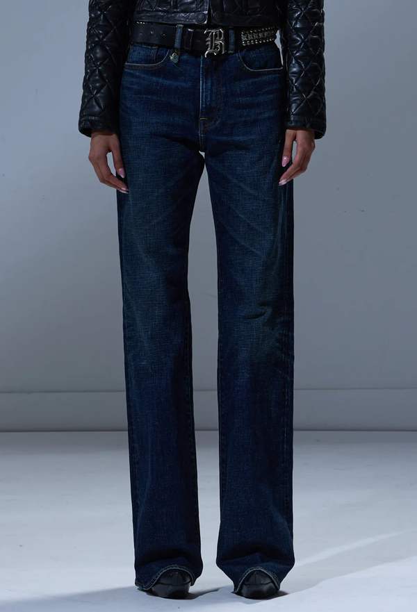 Person wearing dark blue jeans and a black jacket on a plain background